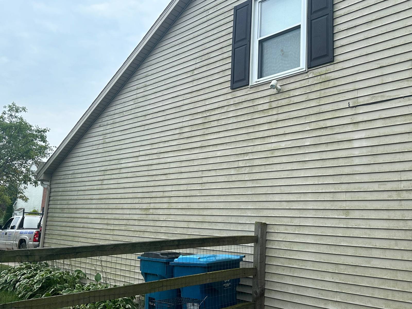 Home gable end before soft washing with visible green algae and mildew streaks on tan siding